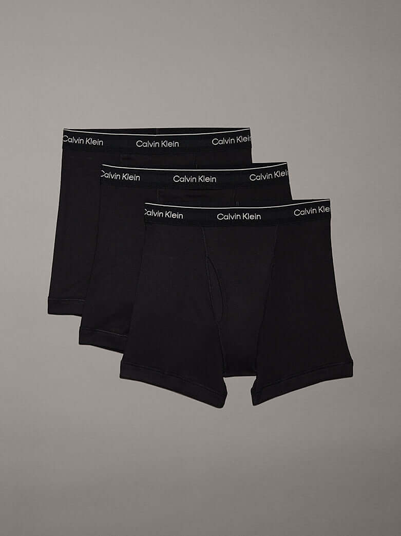 Three pairs of Calvin Klein black boxer briefs on a gray background
