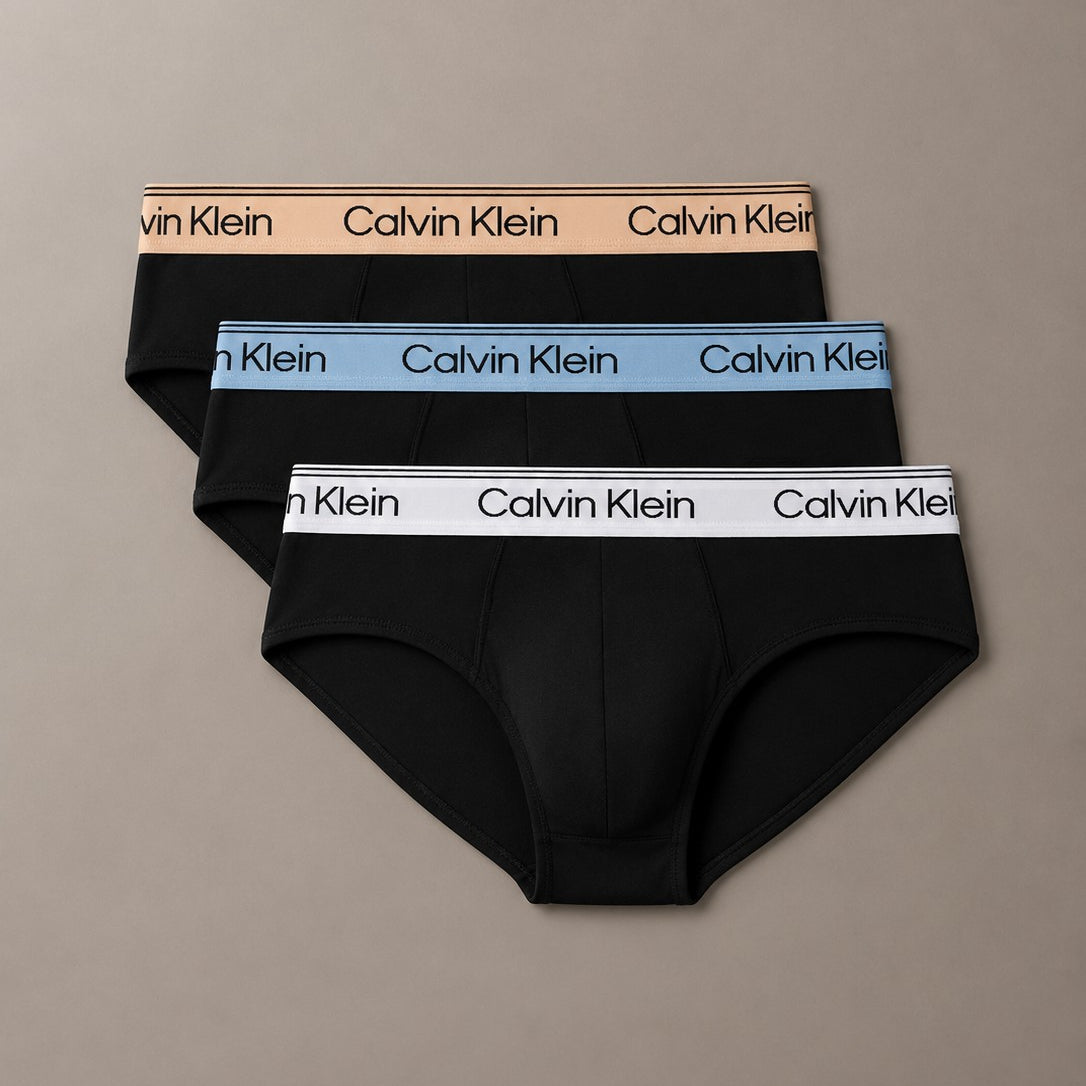 Three pairs of Calvin Klein men's briefs stacked in a fan arrangement on a neutral taupe background. The briefs are black with contrasting elastic waistbands in beige, light blue, and white, each featuring the repeating Calvin Klein logo.