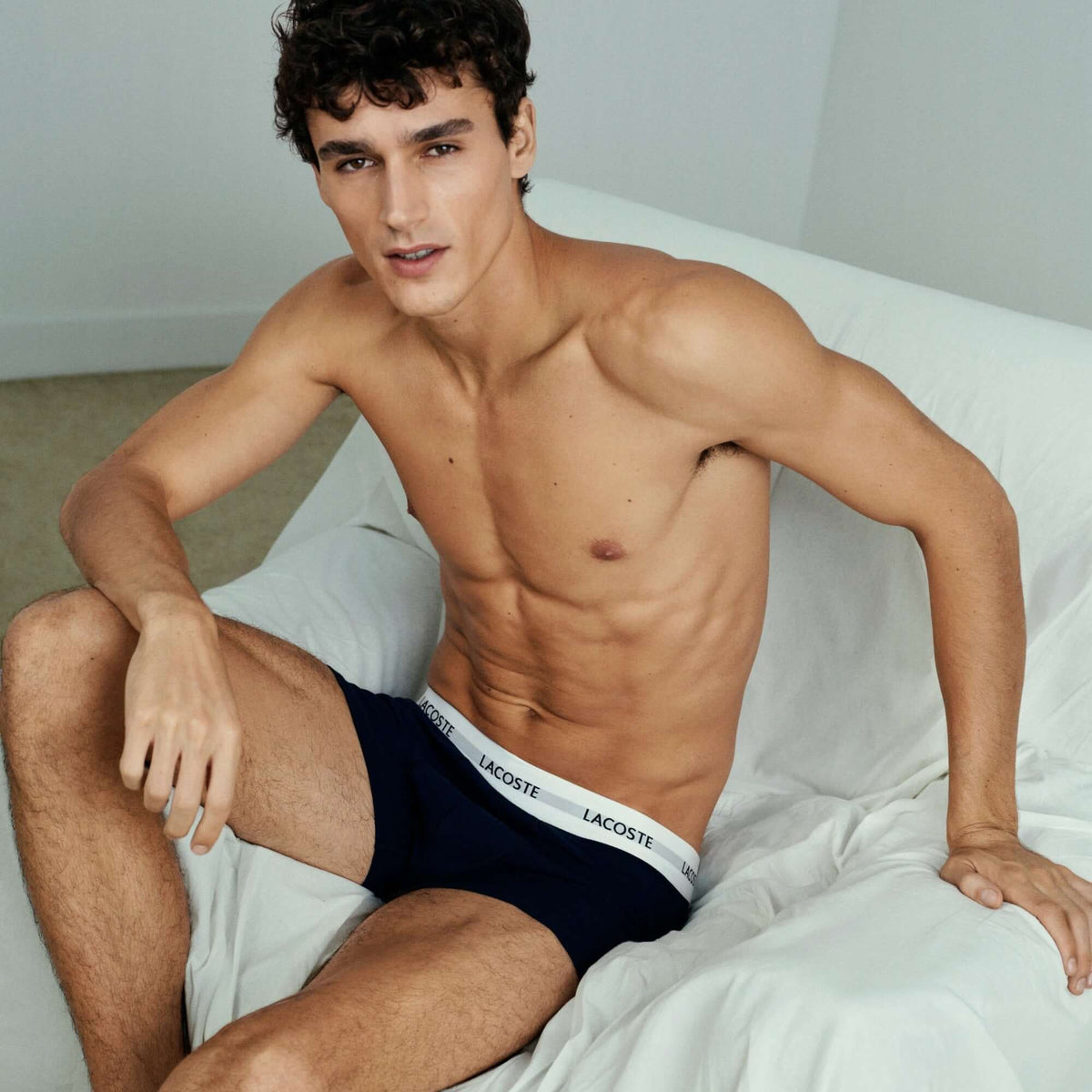 Man wearing Lacoste underwear sitting on a bed