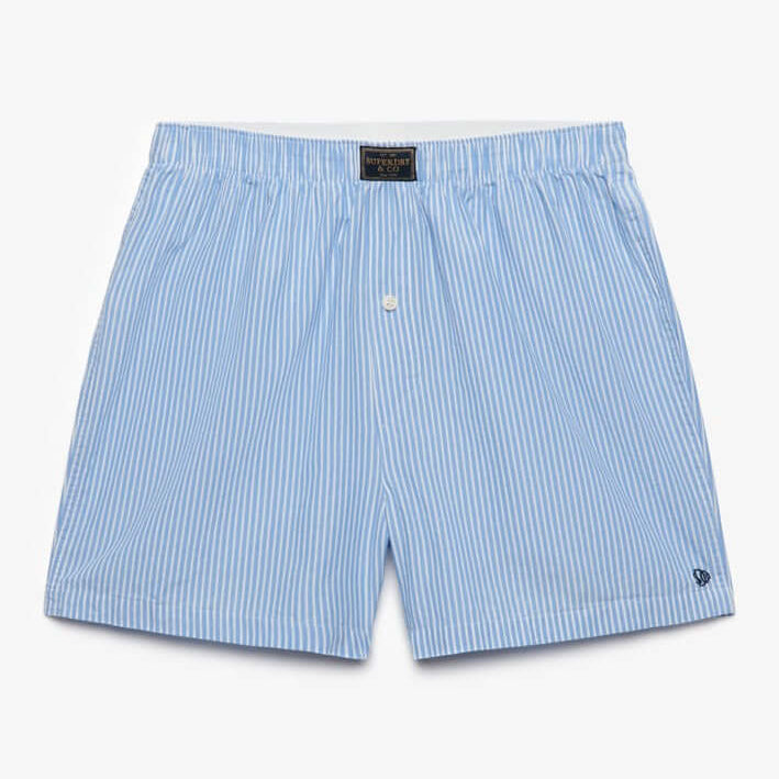 Light blue and white vertically striped boxer shorts with a small white embroidered logo on the lower left hem, displayed flat against a clean white background.