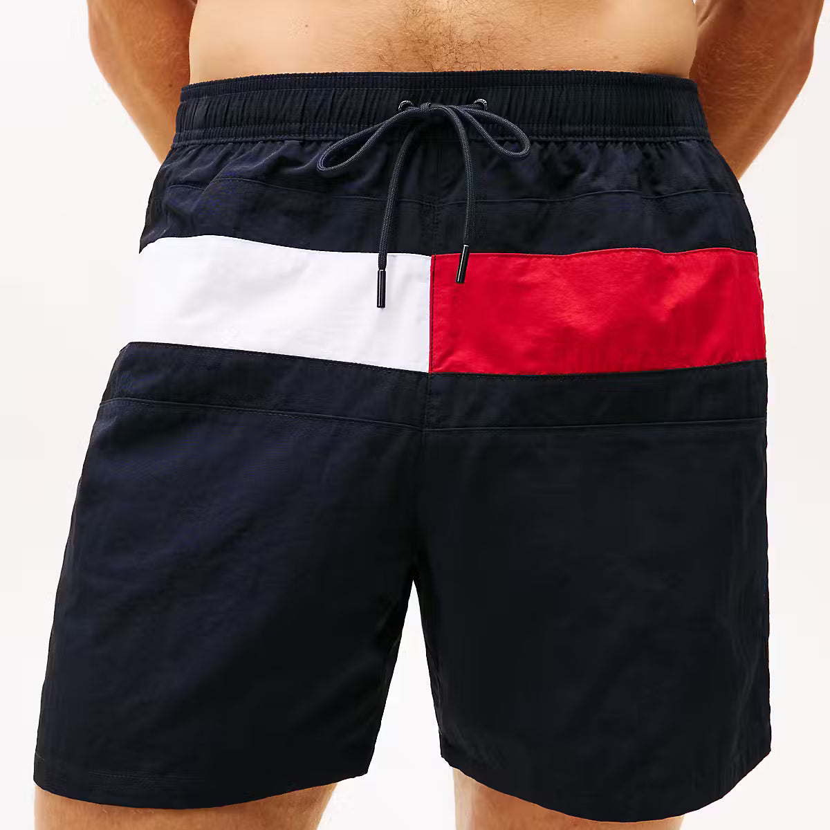 Men's swim trunks featuring a navy blue base with the classic red, white, and navy blue horizontal flag stripe design across the front, shown on a model.