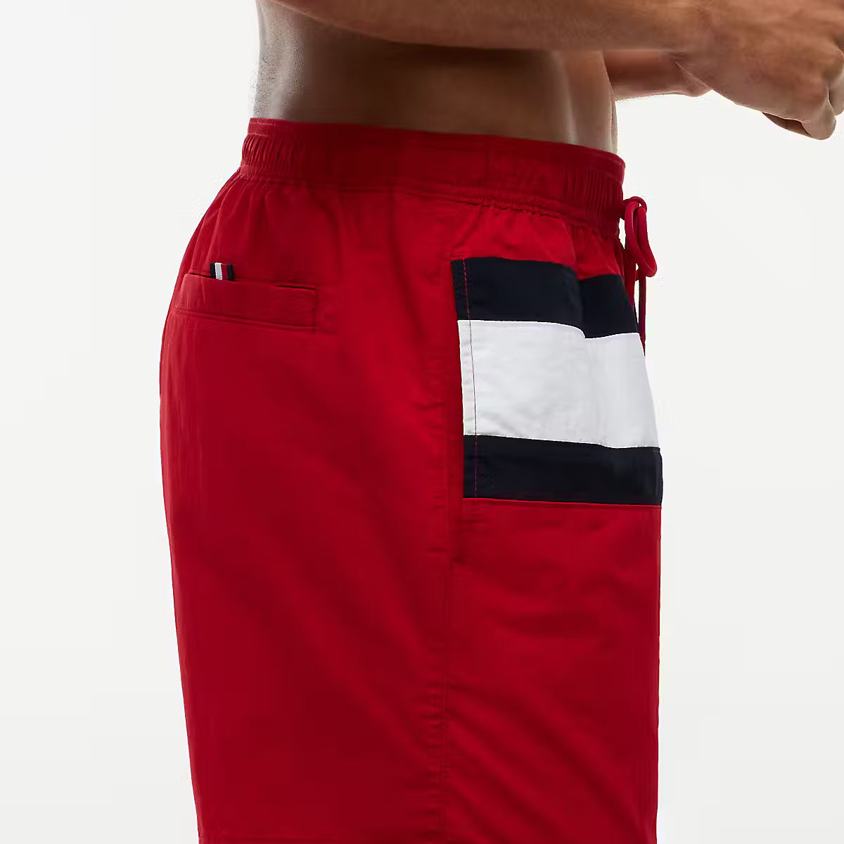 Red swim trunks with a navy and white striped pocket detail, shown on a model against a white background.