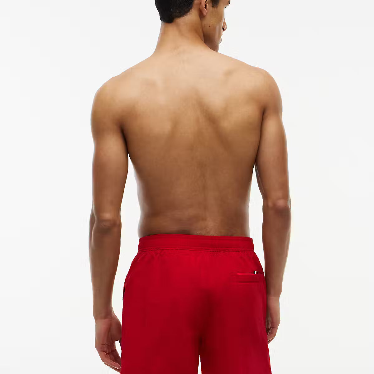A man viewed from behind wearing bright red swim trunks against a clean white studio background.