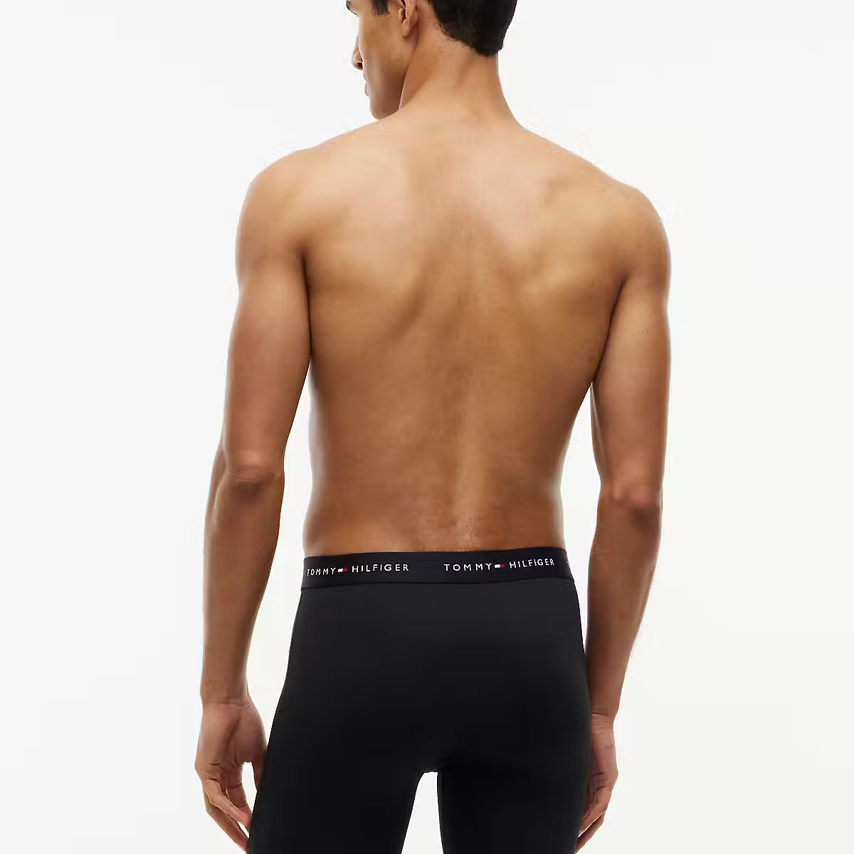A man shown from the back wearing black Tommy Hilfiger boxer briefs against a plain white studio background.
