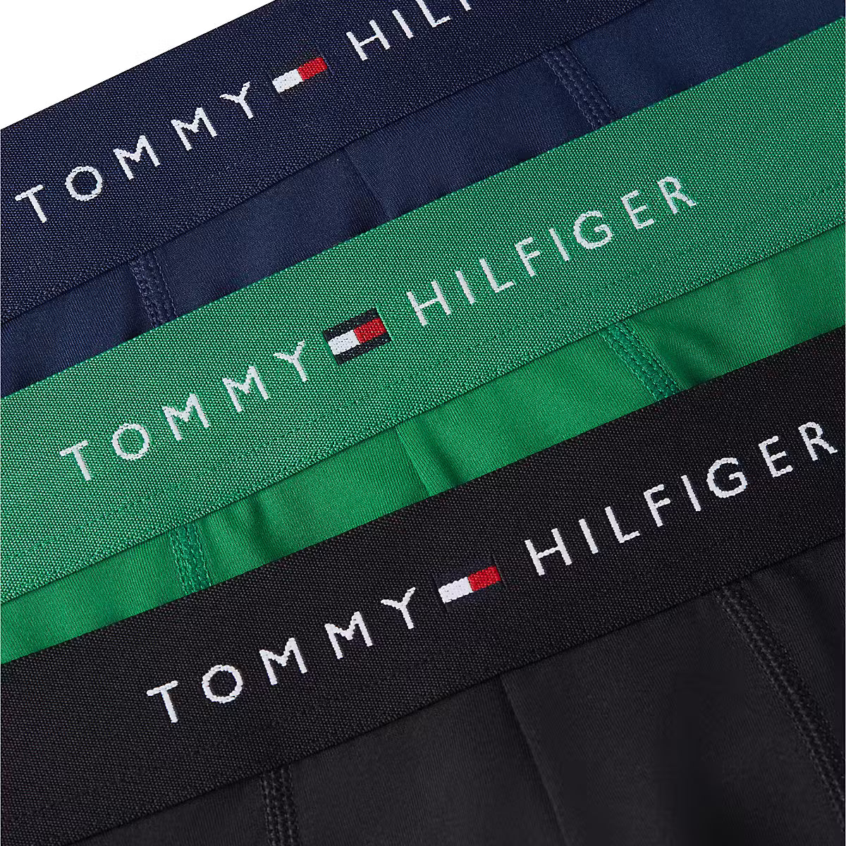 Three Tommy Hilfiger boxer briefs laid flat, showing navy, green, and black waistbands with white TOMMY HILFIGER branding and the small flag logo.