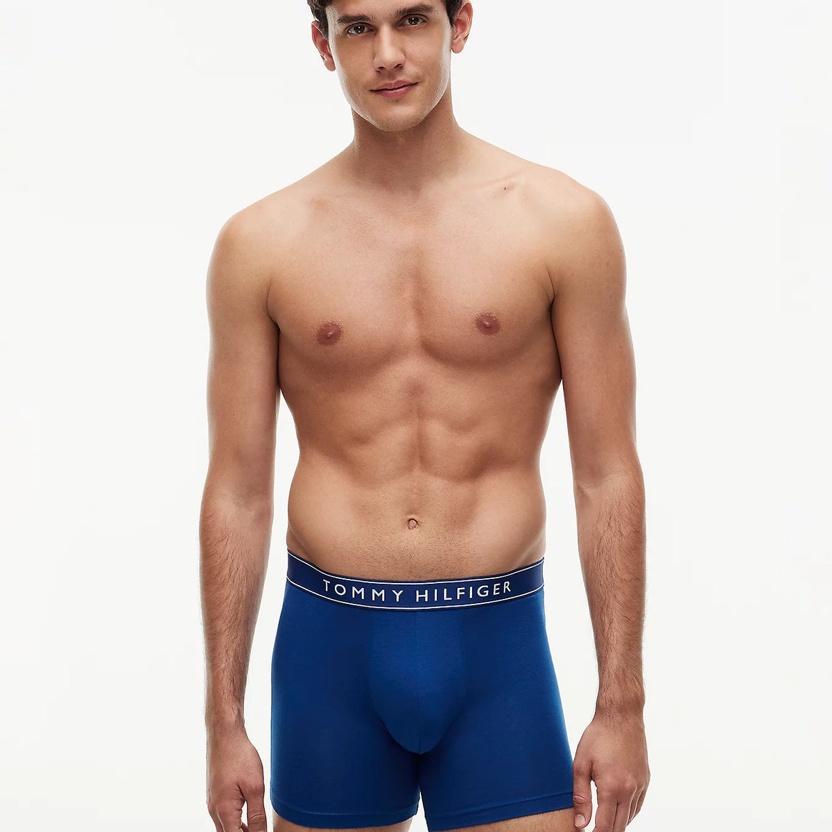 A male model wearing blue Tommy Hilfiger boxers, standing against a plain white studio background.