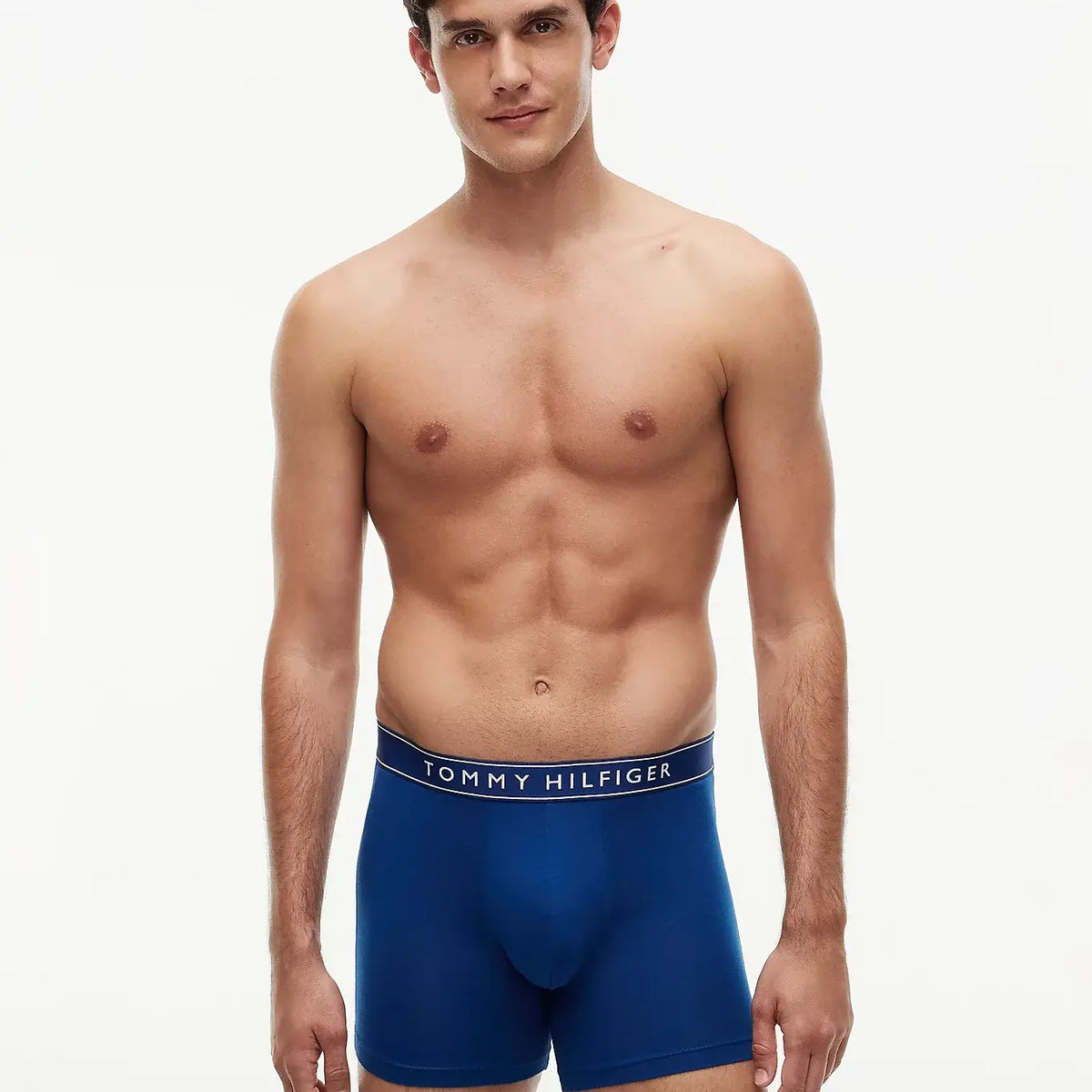 A male model wearing blue Tommy Hilfiger boxers, standing against a plain white studio background.
