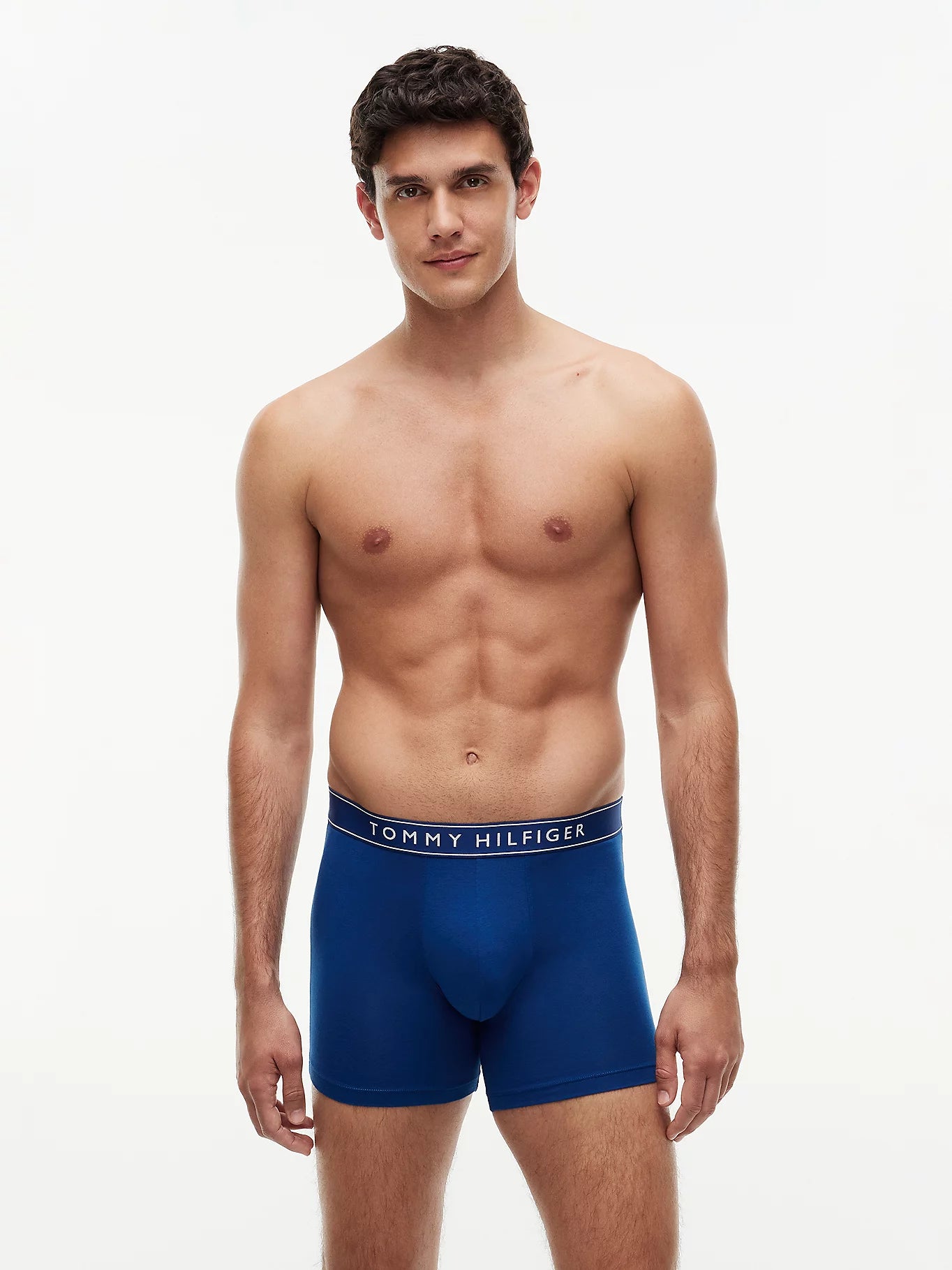 A male model wearing blue Tommy Hilfiger boxers, standing against a plain white studio background.