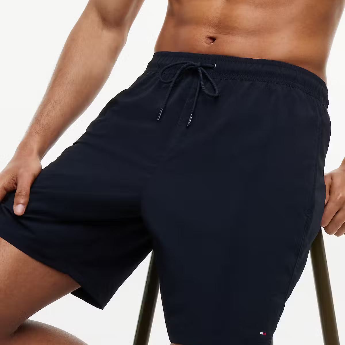 A close-up of a man wearing navy blue swim trunks with a drawstring waist, posed against a clean white background.