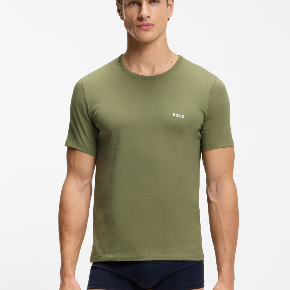 A male model wearing an olive green short-sleeve crewneck t-shirt with a small white BOSS logo on the left chest, paired with navy blue boxer briefs, against a plain light gray studio background.