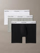 Three pairs of Calvin Klein boxer briefs in black, gray, and white on a beige background.