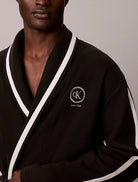 A close-up of a man wearing a dark brown waffle-knit robe with white contrast trim and a white embroidered Calvin Klein logo on the chest.