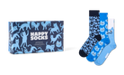 A boxed set of three patterned socks displayed beside the retail box on a light gray background. The packaging and sock designs feature blue cat illustrations and the text 'HAPPY SOCKS'.