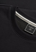 Close-up of a black crewneck sweatshirt showing the ribbed collar, a white stripe detail inside the neckline, and a black Superdry brand label.