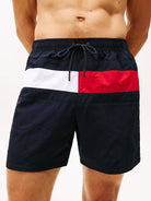 Men's swim trunks featuring a navy blue base with the classic red, white, and navy blue horizontal flag stripe design across the front, shown on a model.