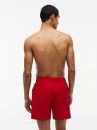 A man viewed from behind wearing bright red swim trunks against a clean white studio background.