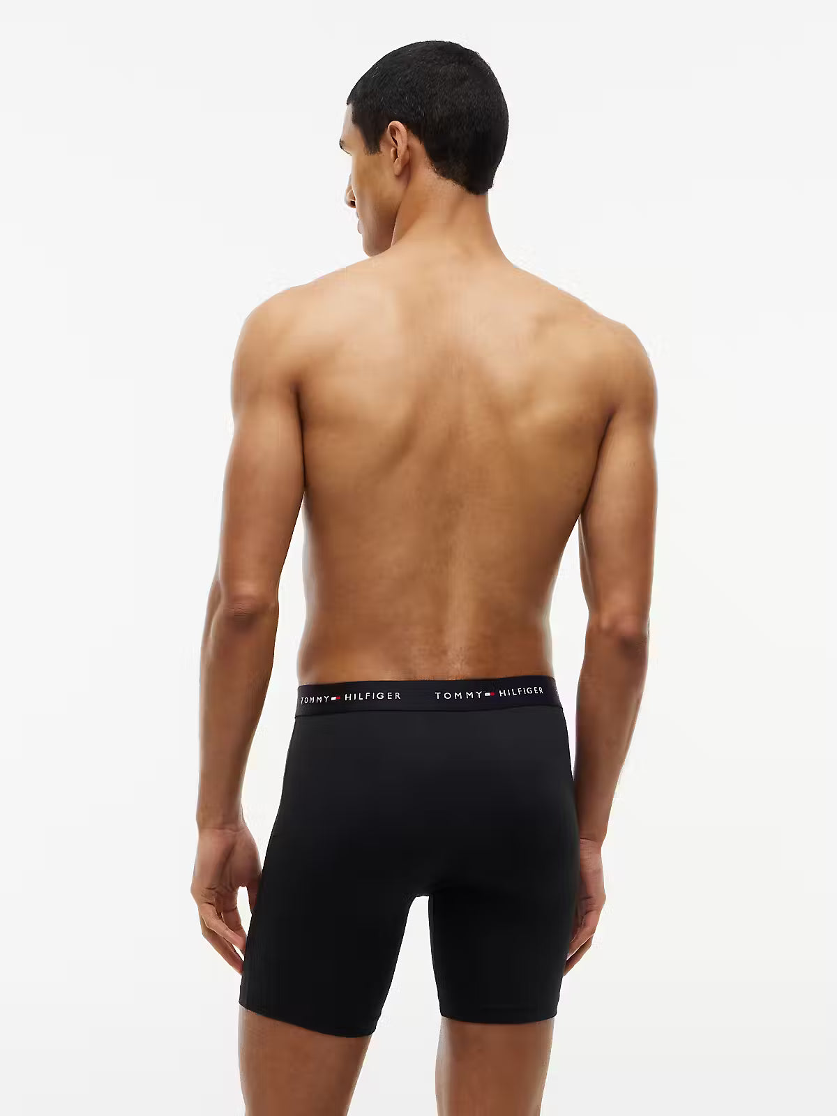 A man shown from the back wearing black Tommy Hilfiger boxer briefs against a plain white studio background.