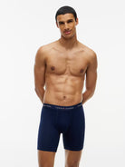 A shirtless male model wearing Tommy Hilfiger navy blue boxer briefs, standing against a plain white studio background.