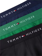 Three Tommy Hilfiger boxer briefs laid flat, showing navy, green, and black waistbands with white TOMMY HILFIGER branding and the small flag logo.