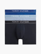 Three pairs of Tommy Hilfiger men's boxer briefs stacked vertically on a light gray background. The top pair is dark blue with white text, the middle pair is light blue with white text, and the bottom pair is black with white text.