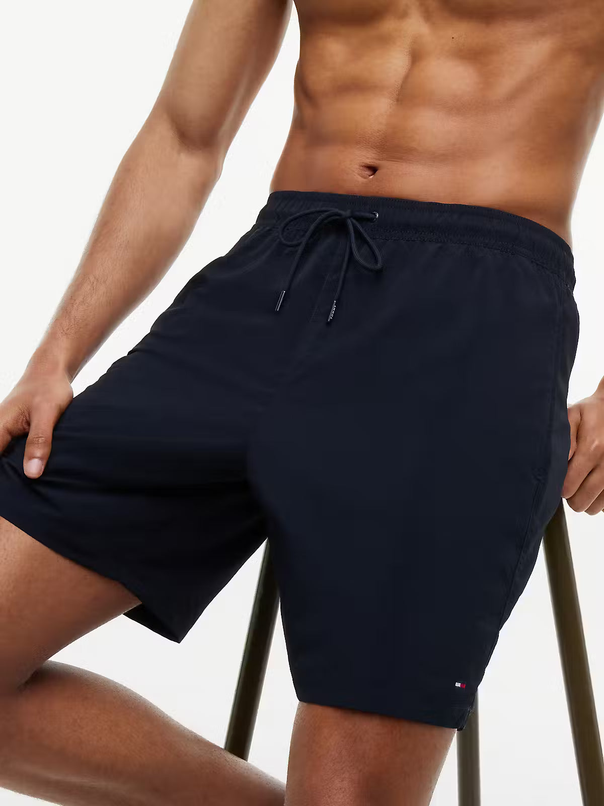 A close-up of a man wearing navy blue swim trunks with a drawstring waist, posed against a clean white background.